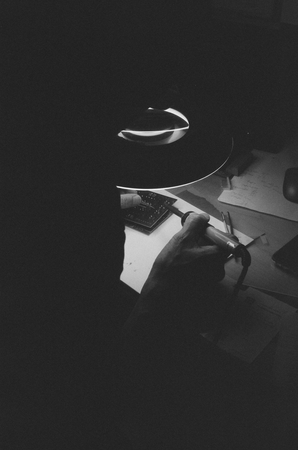 Close-up of soldering work on a circuit board under a bench lamp